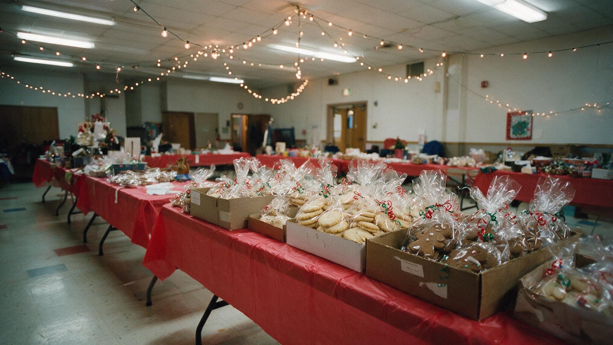 Tables of cellophane-wrapped shortbread and gingerbread cookies at a community holiday bazaar in a church hall